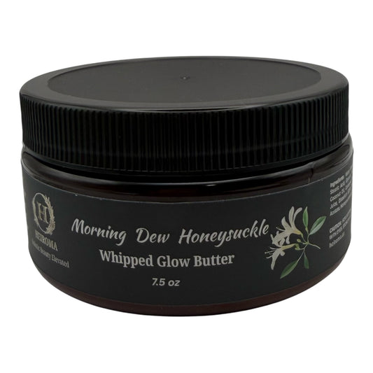 A jar of Morning Dew Honeysuckle Whipped Glow Butter by Heiroma. The product is in a dark amber glass jar with a black ribbed screw-on lid and a black label featuring white text and a small white flower illustration.